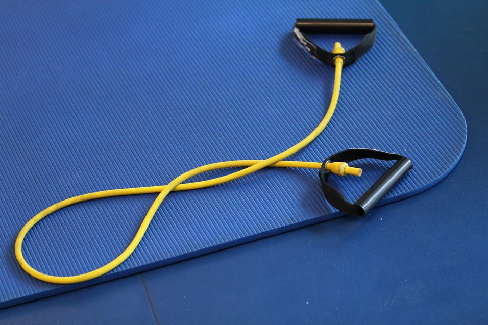 Gelbes Widerstandsband mit schwarzen Griffen auf einer blauen Gymnastikmatte.